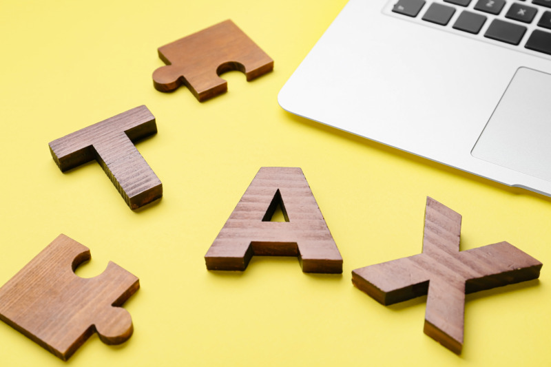 Word TAX with puzzle pieces and laptop on color background_Adobe Stock_20240102